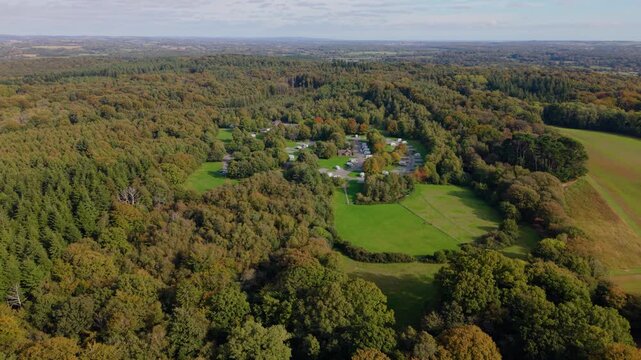 Rookesbury Park Caravan and Motorhome Club site Wickham Hampshire very high backwards drone flight revealing setting in the Bere Forest in bright sunlight with early Autumn trees