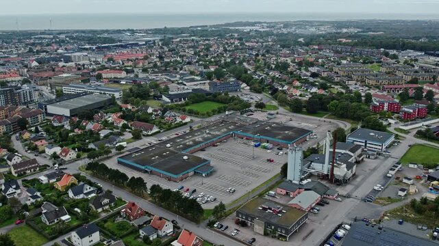 Drone shot over the industrial district of Falkenberg, Sweden. Large warehouse buildings and a factory chimney in the foreground, with residential streets, green areas and the sea on the horizon.