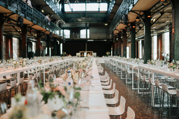 Elegant wedding reception in historic industrial hall, banquet long tables flowers