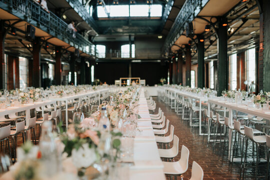 Elegant wedding reception in historic industrial hall, banquet long tables flowers