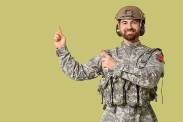 Naklejka premium Young happy male soldier in uniform pointing at something on green background
