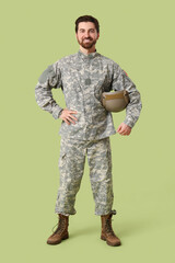 Naklejka premium Young happy male soldier in uniform with helmet on green background