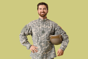 Naklejka premium Young happy male soldier in uniform with helmet on green background