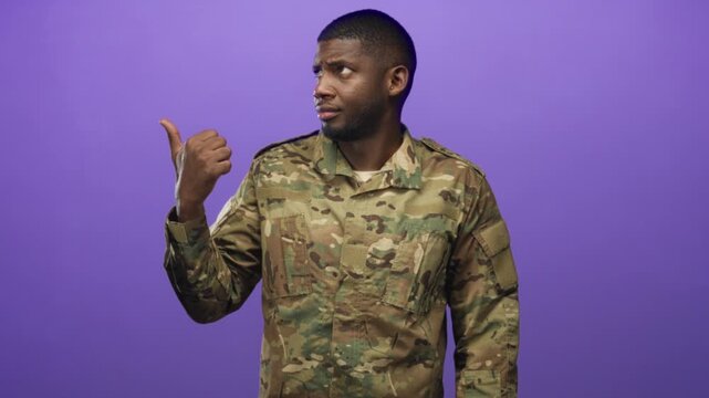 Man in camouflage military uniform points thumb over shoulder in studio with purple backdrop and questioning look; doubt direction.