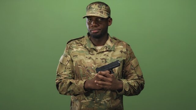Man soldier in camouflage uniform and cap holding pistol with both hands in a studio green screen setting; duty focus vigilance.