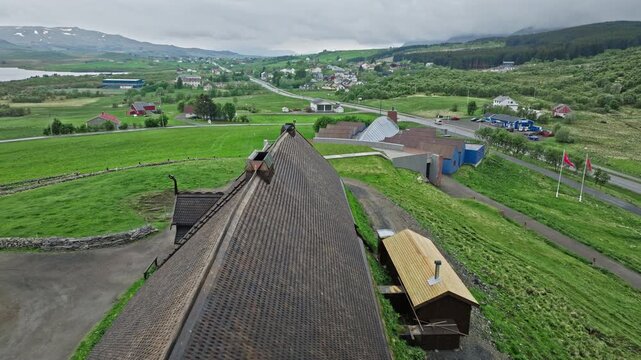 Drone view flying above the reconstructed Viking longhouse at Lofotr Viking Museum in Borg, Lofoten Islands, Norway. Historic Norse architecture set within scenic rural landscape of northern Norway.