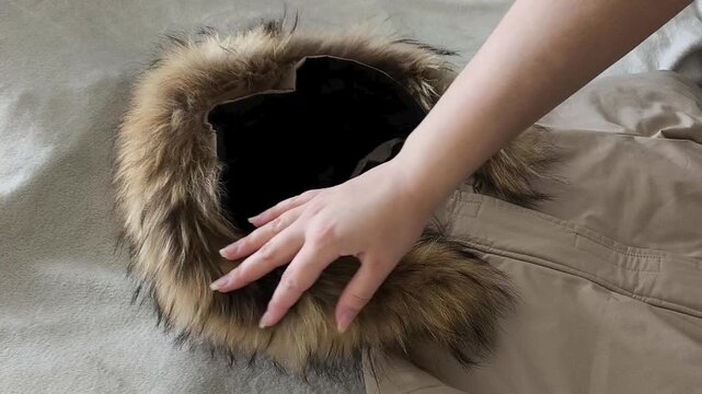 A woman's hand touches the fluffy fur on the hood of her jacket. Natural or artificial eco fur on the collar of the coat. Warm clothes