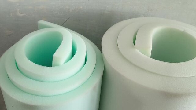 A rolled roll of white foam rubber against the background of a grunge wall. Repair, insulation of walls. Filler for upholstered furniture