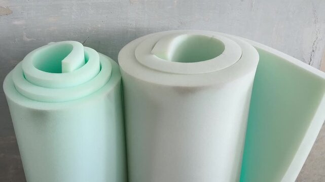 A rolled roll of white foam rubber against the background of a grunge wall. Repair, insulation of walls. Filler for upholstered furniture