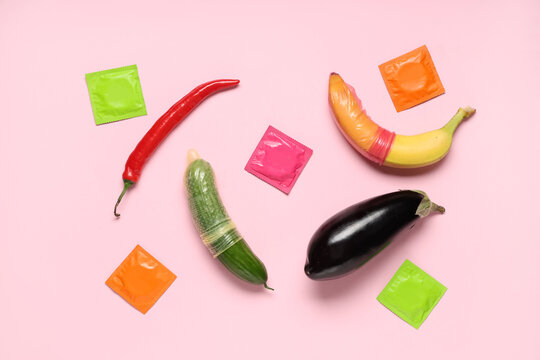 Condoms with fruits and vegetables on pink background. Sex education