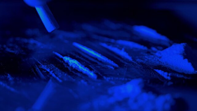 Close up white powder lines on reflective surface illuminated by deep blue light