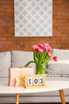 Vase with flowers, gift box and calendar on coffee table in living room