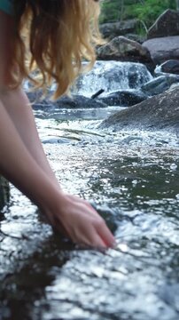 Young woman drinking fresh water from a clean forest stream in summer. Pure nature, peace, and refreshment. A quiet moment in the wilderness, symbol of connection with nature and natural living.