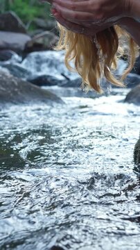 Young woman drinking fresh water from a clean forest stream in summer. Pure nature, peace, and refreshment. A quiet moment in the wilderness, symbol of connection with nature and natural living.