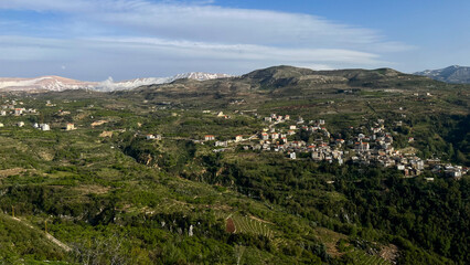 Fototapeta premium Panoramic view of a mountainous landscape with a small village nestled among lush greenery and rolling hills under a clear blue sky in Lebanon's Beqaa Valley region
