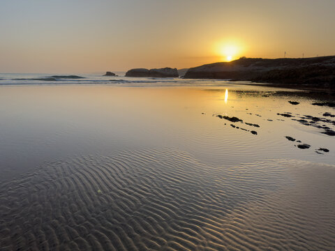 Ripples in wet sand reflecting sunrise light on empty Atlantic beach calm ocean morning minimal coastal landscape Cantabria Santander Virgen del Mar Spain