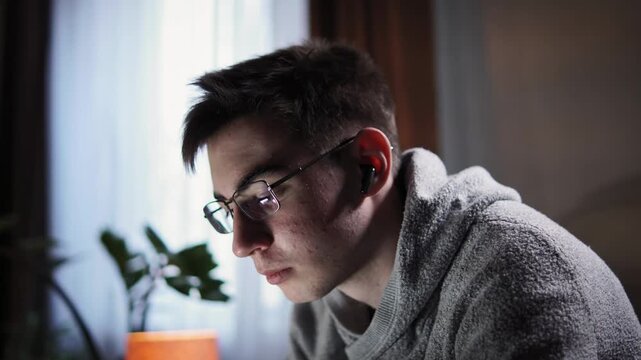 Teenager like nerd wearing glasses sits on sofa in background light from window