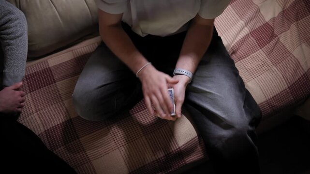 A man sitting on a sofa with a deck of cards in his hands shows card tricks