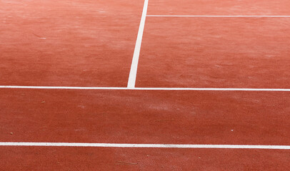 A clay court, marked with bright white lines, awaits the next set. Tennis balls scattered across the surface hint at a recent practice. Greenery surrounds the outdoor space.