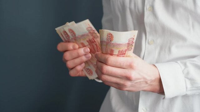 A close-up of a man's hands counts a bundle of bills for five thousand Russian rubles. Man counts red paper 5000 rubles bills. Russian cash money in male hand. A man holds a wad of money in his hands.