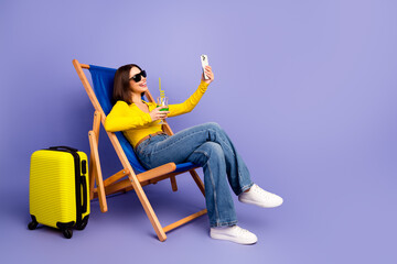 Happy chic young woman lounging in a bright yellow outfit takes a selfie on a purple background...