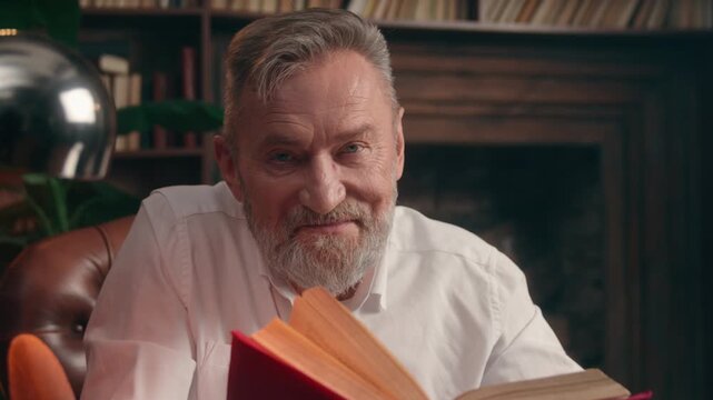 Caucasian old senior business man reading book taking off glasses looking at camera smiling happy aged elderly retired businessman male specialist relaxed literature smile positive posing at office