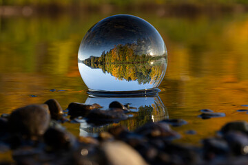 A colorful image of a photographic lens ball reflecting an inverted image of brightly colored leaves surrounding Shawinigan Lake, British Columbia, Canada.