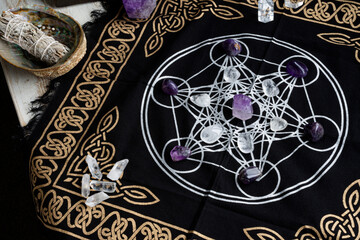 A top view image of a crystal healing grid using clear quartz and amethyst crystals along with white sage smudge stick and grid cloth. 