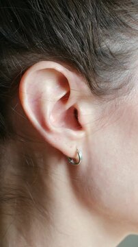 Close up young caucasian woman wiggling her ear, showing unique and funny talent. Girl has dark hair and wears small silver earring on her pierced earlobe. Young woman wiggling ear with special skill