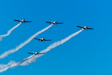 Airshow performance with aircraft, flight of pilotage team with colorful smoke trails. Planes and jets in the air. Flight show of air force team with group of planes in blue sky.