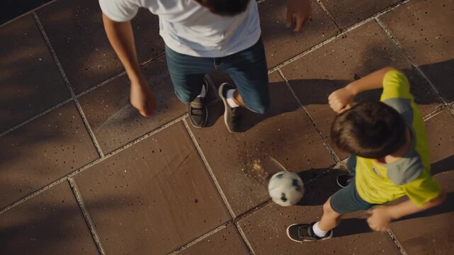 Ball descending, father and son practicing soccer ball control on sunlit tiled patio, white polo