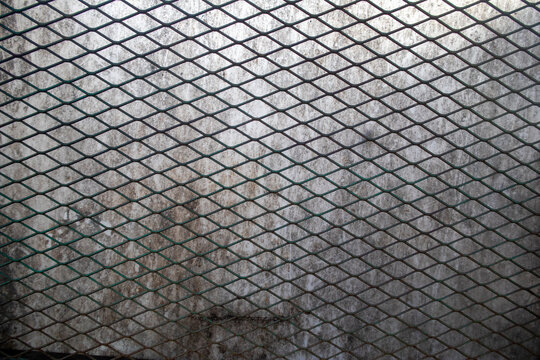 Industrial expanded metal mesh screen with a diamond pattern overlaid on a weathered, translucent surface.