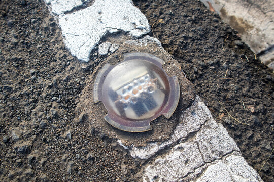 Close-up of a circular solar road stud reflector embedded in asphalt next to a white traffic line.