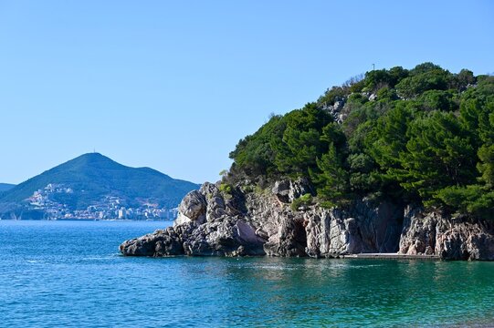 Layered limestone cliffs with green pine trees hanging over the turquoise Adriatic Sea.