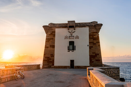 beautiful sunset or sunrise at beautiful embarkment with nice tower on a cape point of a promontory among blue sea vawes. Urban dock pier in golden evening sunset rays leading to a scenic tower.