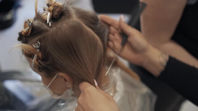 Close up of a hair stylist sectioning a woman's brown hair with silver clips in a salon during a coloring treatment
