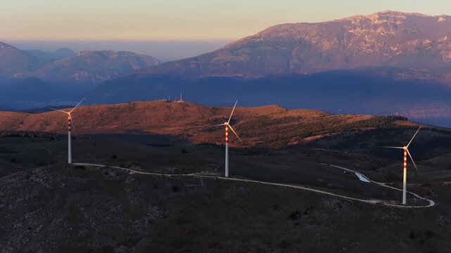 Aerial view of several wind turbines standing tall on a hill, with mountains in the background, Cocullo, Abruzzo, Italy.