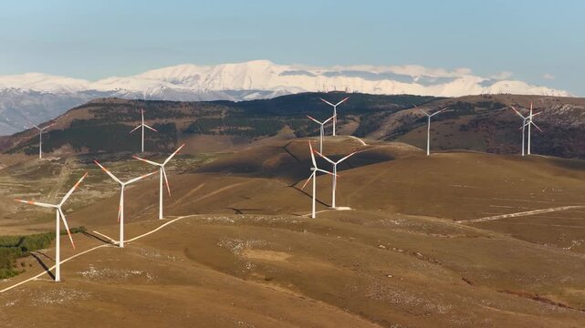 Aerial view of wind turbines standing tall on hills, with snowy mountains in the background, Cocullo, Abruzzo, Italy.