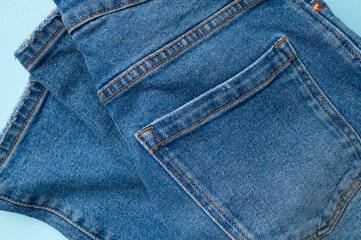 Fototapeta premium Blue jeans on light blue background flat lay top view. Denim, stylish casual pants, natural cotton fabric. Clothing concept, fashion, shopping, in-store sale, discounts