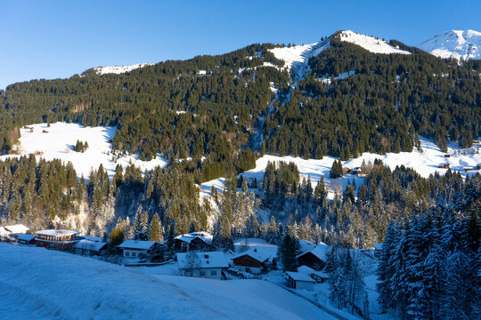 Alpine Schneelandschaft mit Bergh&uuml;tten und schneebedeckten B&auml;umen im Kleinwalsertal, beliebte Region f&uuml;r Winterurlaub.
