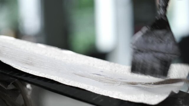 Hairdresser applying bleach to hair sections on foil using a tint brush