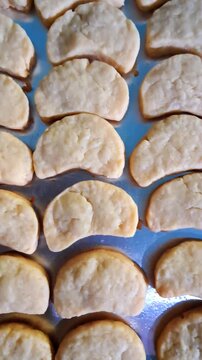 Top view of homemade crescent-shaped butter cookies on a baking tray, traditional Indonesian Putri Salju cookies before icing