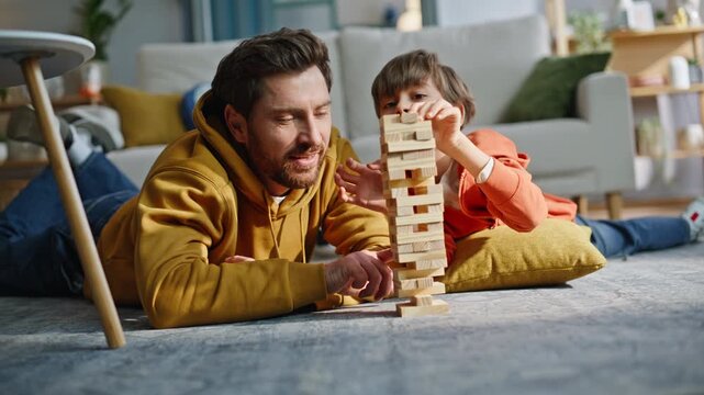Daddy kid enjoy jenga lying floor closeup. Playful little son building toy tower