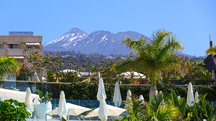 luxury seaside resort on tenerife framed by tall palms and bright umbrellas, opening toward the distant snow‑touched summit of pico de teide rising above the landscape with a calm and expansive island © Gabriela
