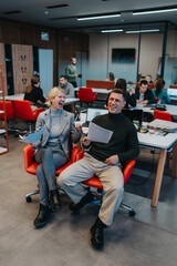 Two coworkers laugh together while holding papers in a bright, modern office during a team session.