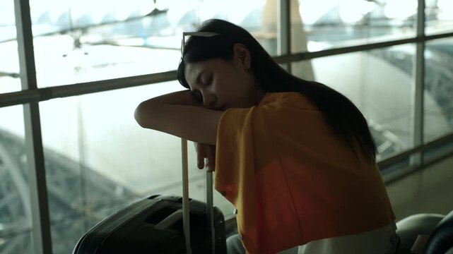 Tired young sola woman traveler sleeping on airport waiting chairs while holding smartphone and boarding pass after long flight delay, bored passenger waiting at airport terminal.
