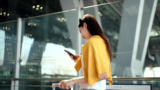 Happy woman solo traveler walking at the airport  holding smartphone, passport and boarding pass ready for vacation. Travel lifestyle, digital travel planning and travel insurance concept.
