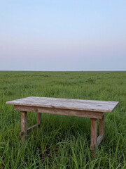 Rustic Wooden Table Standing Alone in a Vast Green Field at Sunrise or Sunset with Soft Natural Light and Serene Countryside Atmosphere