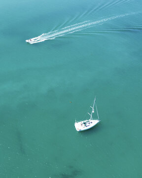 Aerial view of a sailboat and motorboat cutting through the turquoise waters, leaving white wakes in their paths, Manche, Normandy, France.
