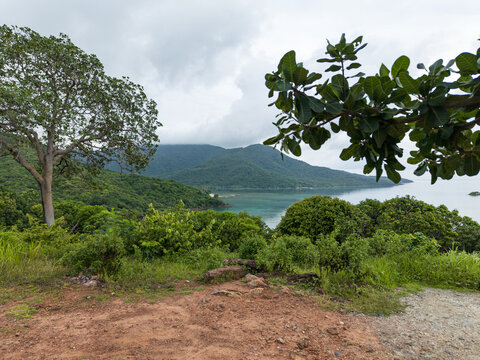 Aerial view of turquoise waters meet lush green hillsides under a cloudy sky, a serene coastal vista unfolds, Karimunjawa, Central Java, Indonesia.
